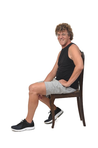 Side view of a man with sportswear sitting on chair and smiling and looking at camera on white