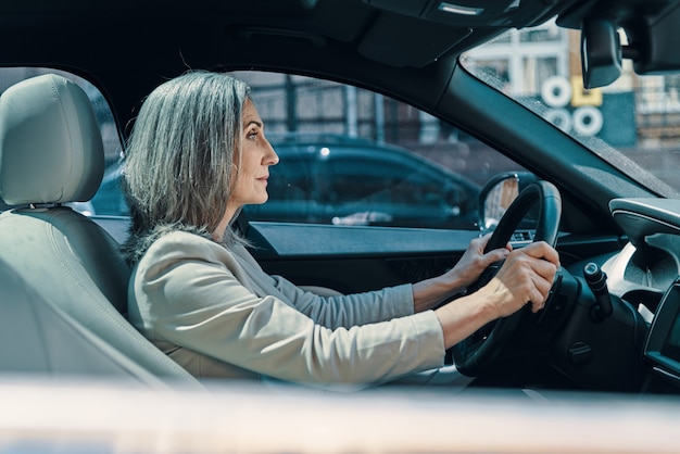 Side view of mature beautiful woman in smart casual wear smiling while driving car