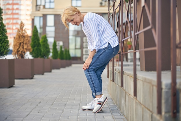 Side view of a mature Caucasian lady suffering from the joint pain in the street