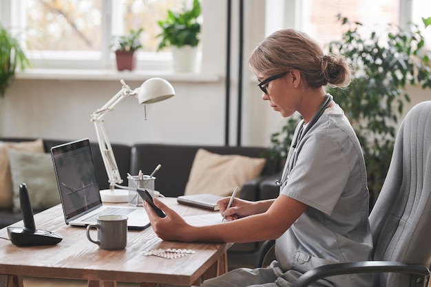 Side view medium shot of young adult female therapist sitting at desk in front of laptop holding sma