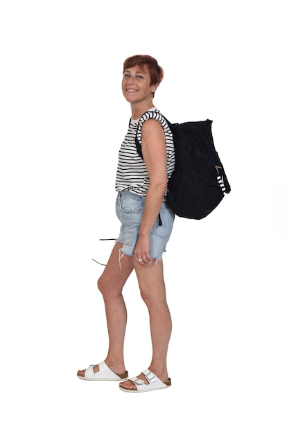 Side view of a middle aged woman on a summer day with backpack lookig at camerra on white background