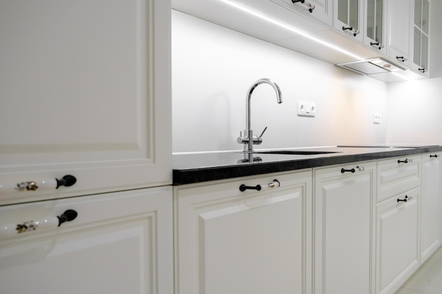 Side view modern and elegant kitchen with white drawers and cupboards black marble countertop and builtin sink with silver tap