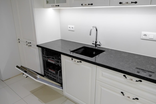 Side view modern and elegant kitchen with white drawers and cupboards black marble countertop and builtin sink with silver tap