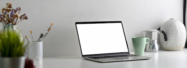 Side view of modern office desk with blank screen laptop, painting tools and decorations