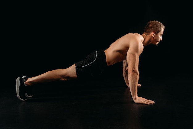 Side view of muscular sportive bodybuilder doing push ups isolated on black