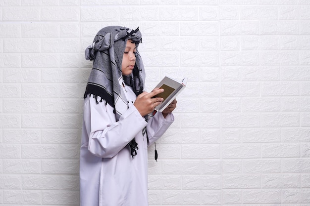 Side view of muslim kid wearing arabian style and turban reciting quran