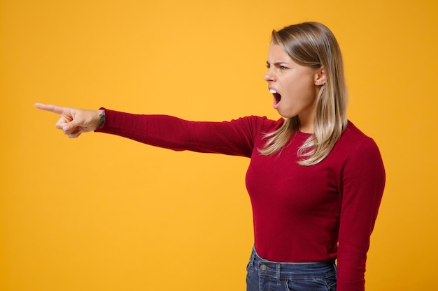 Side view of nervous young blonde woman girl in casual clothes posing isolated on yellow orange background in studio. People lifestyle concept. Mock up copy space. Point index finger aside, swearing.