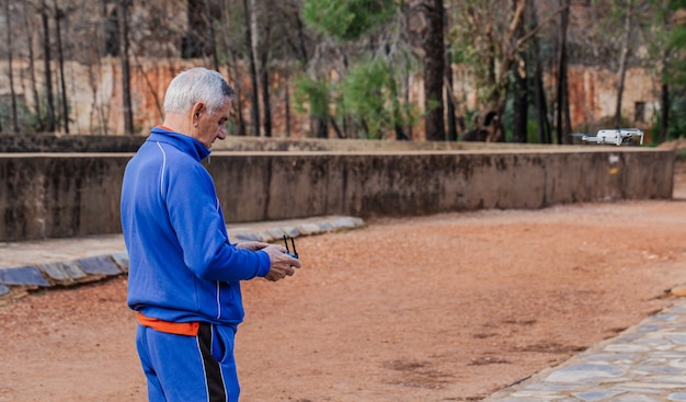 Side view of old man flying the drone in sportswear