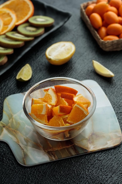 Side view of orange slices in bowl with kiwi slices and kumquats with lemon and lime slice on black background