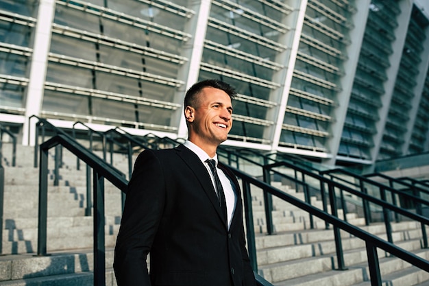 Side view photo of confident businessman in formal wear looking away while walking down on stairs