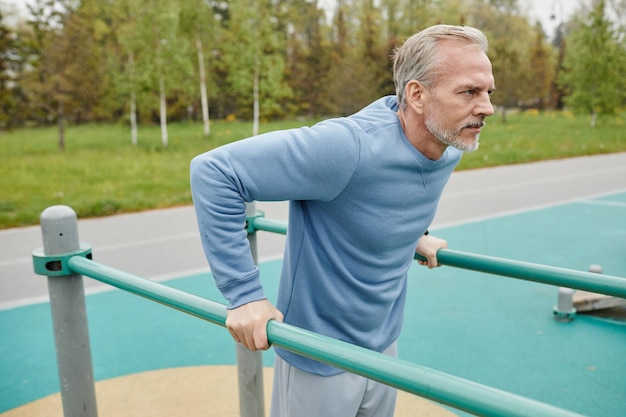 Side view portrait of active mature man exercising on parallel bars outdoors copy space