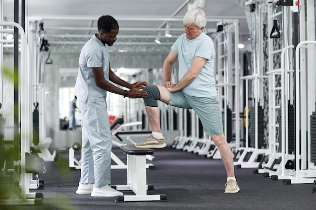 Side view portrait of african american therapist assisting senior man at gym in rehabilitation clini