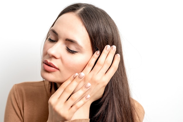 Side view portrait of beautiful young caucasian brunette woman with closed eyes touching her hair by manicured fingers on white background