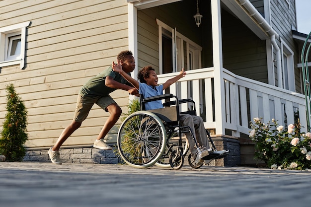 Side view portrait of black teenage boy pushing littlle brother in wheelchair while having fun toget