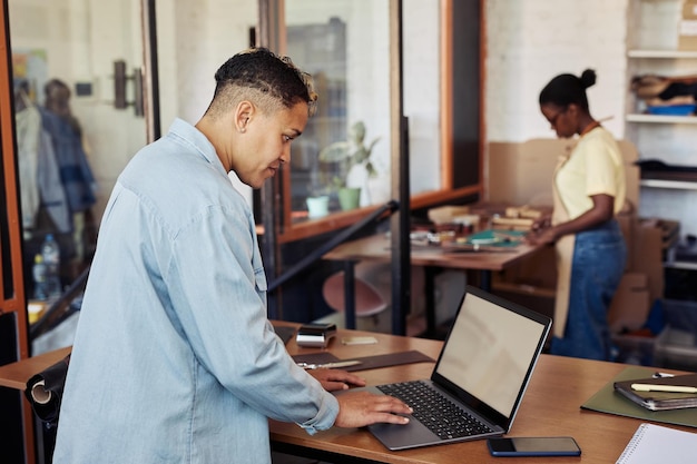 Side view portrait of female small business owner using laptop in leatherworking workshop copy space