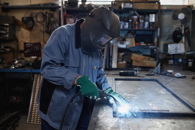 Side view portrait of female welder working with metal in industrial workshop copy space