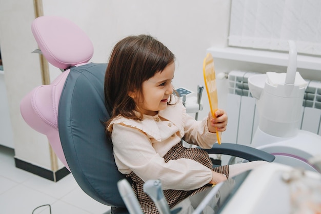 Side view portrait of little girl looking at mirror in pediatric dentistry after dental surgery.