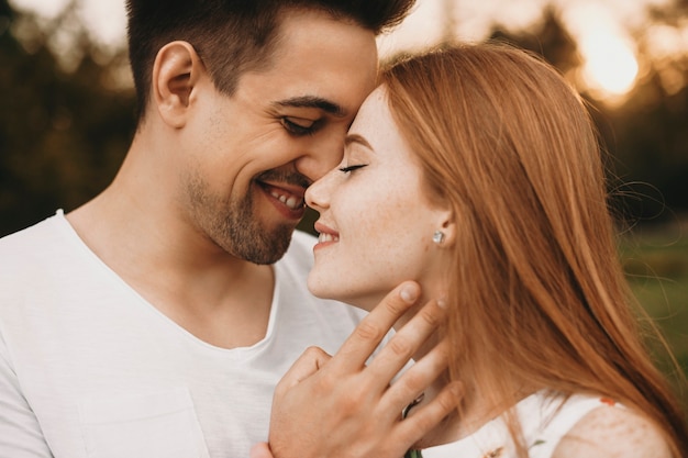 Side view portrait of a lovely couple dating outside face to face with closed eyes smiling before kissing while is touching face of his friend.