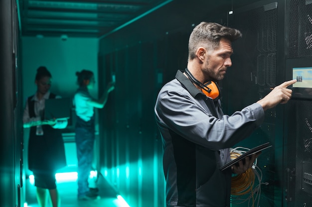 Side view portrait of male network engineer using control panel while operating server in data center, copy space