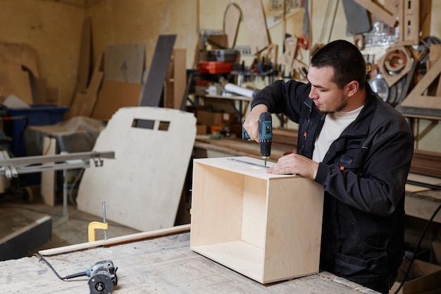 Side view portrait of male worker building wooden furniture in factory workshop copy space