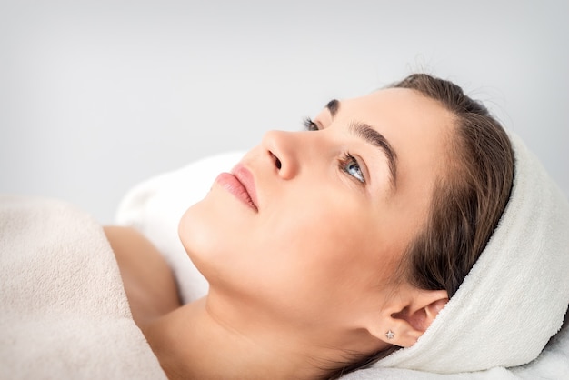 Side view portrait of pensive young woman lying on beautician table while waiting for cosmetic procedure in beauty salon