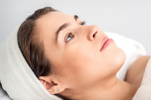 Side view portrait of pensive young woman lying on beautician table while waiting for cosmetic procedure in beauty salon