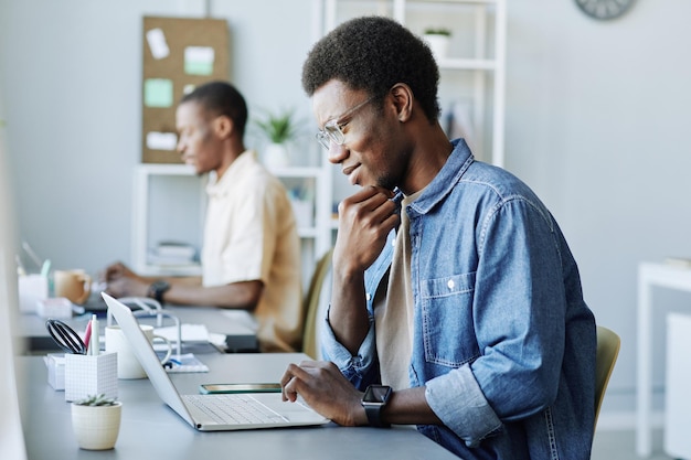 Side view portrait of smiling black man using laptop computer while working in it office copy space