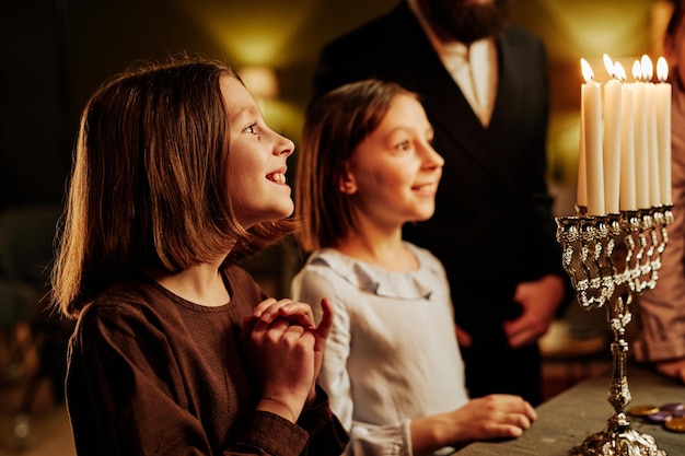 Side view portrait of smiling jewish girls looking at menorah candle during hanukkah celebration cop