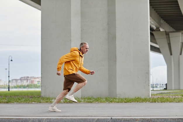 Side view portrait of sportive mature man running fast in urban setting while wearing bright yellow