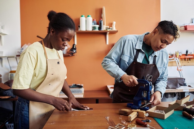 Side view portrait of two multiethnic young women working with leather in workshop and creating hand