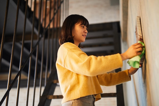 Side view portrait of young Asian woman cleaning house in sunlight copy space