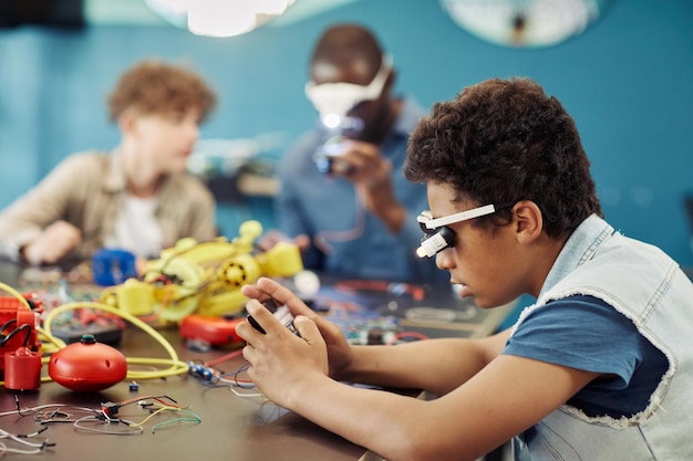 Side view portrait of young black boy building robots in engineering class at school copy space