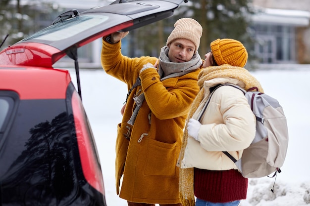 Side view portrait of young couple opening car trunk in winter while travelling for holidays