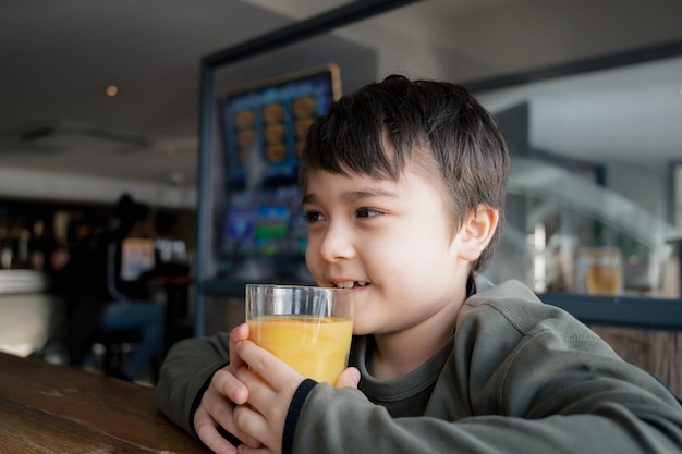 Side view Portrait Young kid drinking fresh orange juice for breakfast in cafe Happy child boy drinking glass of fruit juice while waiting for food in restaurant Healthy food lifestyle concept