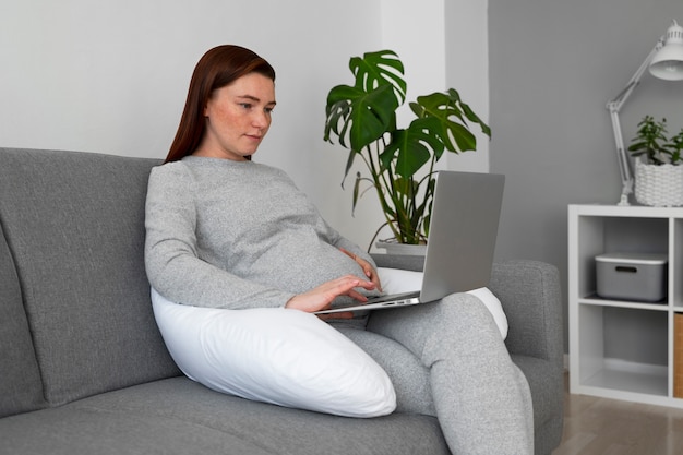 Side view pregnant woman with laptop at home