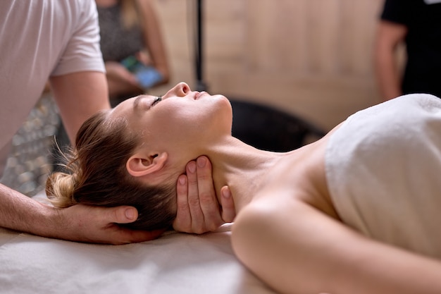 Side view on professional cropped therapist doing healthy massage on neck and shoulders to female client lying on back, side view. at spa salon