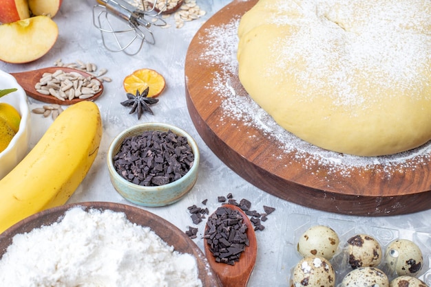 Side view of raw pastry flour on round board grater fresh fruits eggs on gray background