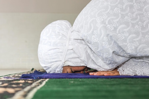 Side view of religious Asian Muslim woman pray to God in Sujud posture on prayer mat