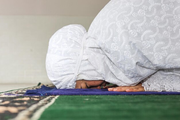 Photo side view of religious asian muslim woman pray to god in sujud posture on prayer mat