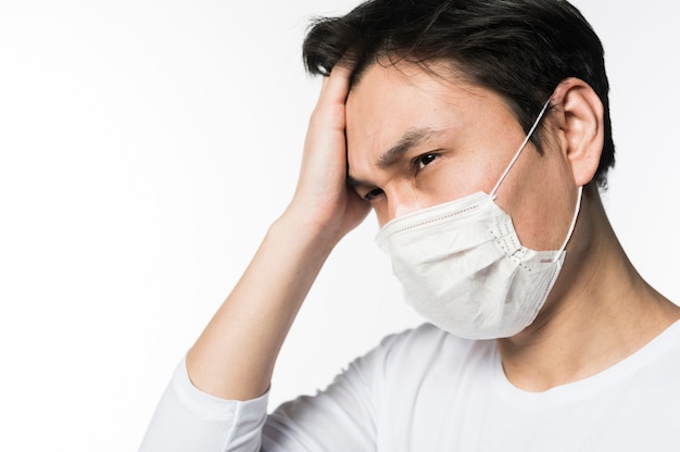 Side view of sad man touching his head while wearing medical mask