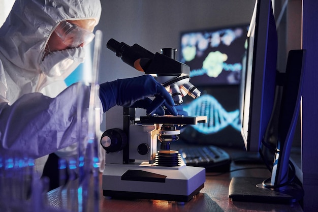 Photo side view of scientist in white protective uniform that works with coronavirus in laboratory