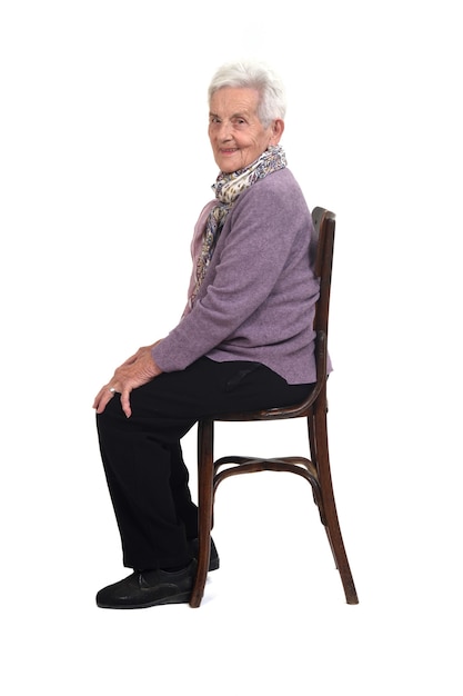 Side view of a senir woman sitting on chair smiling and looking at camera on white background