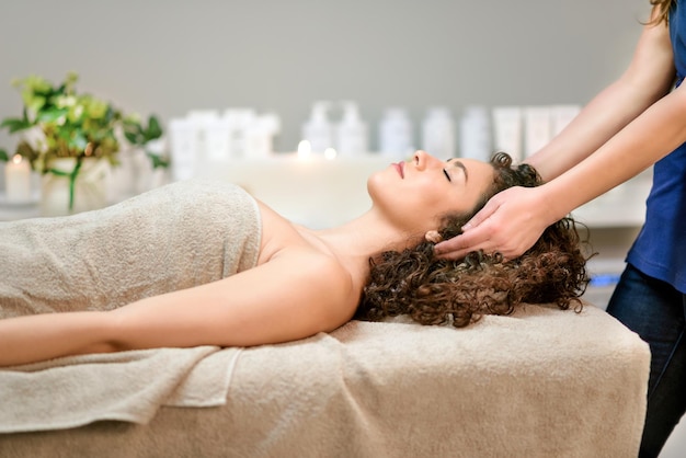 Side view of serene female client with closed eyes wrapped in towel lying on couch and enjoying massage in beauty salon during relaxing procedure