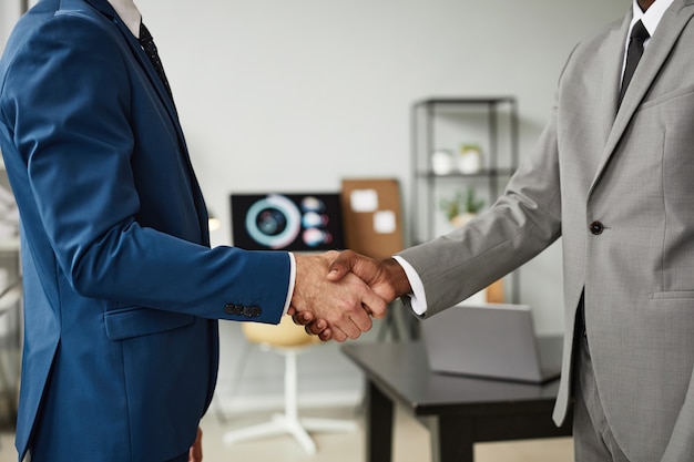 Side view shot of two businessmen shaking hands after successful deal in office copy space