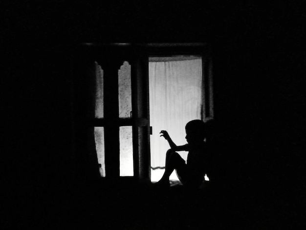 Photo side view of silhouette boy seated against window