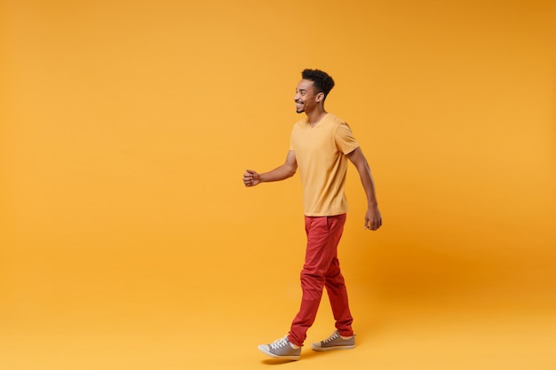 Side view of smiling cheerful young african american guy in casual clothes posing isolated on yellow orange wall  portrait. People sincere emotions lifestyle concept. 