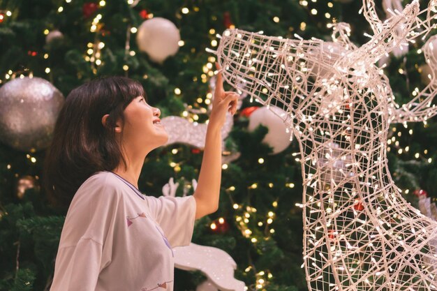 Photo side view of smiling girl looking at illuminated christmas decoration at home