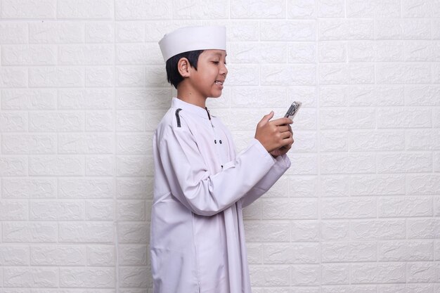 Side view of smiling muslim kid holding smartphone learning koran on application