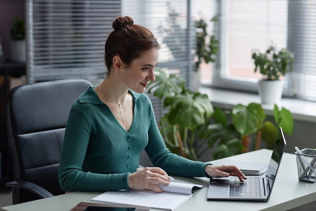 Side view smiling young woman working in cozy office decorated with green plants