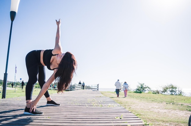 Side view standing woman stretching muscles outdoors touching one foot with one hand copy space